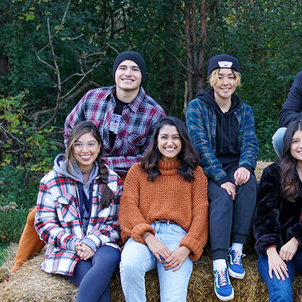 Students with Student Community of Progressive Empowerment (SCOPE) sitting on hay bales at an outdoor fall event