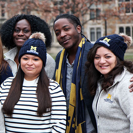 A group of people wearing CEW+ maize and blue gear in the fall at the Law Quad
