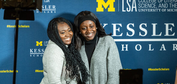 Two students pose for a photo in front of a Kessler Scholars photo wall