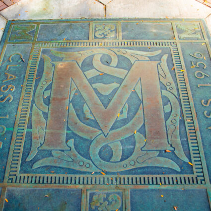 An ornate block M plaque in the sidewalk from the Class of 1956