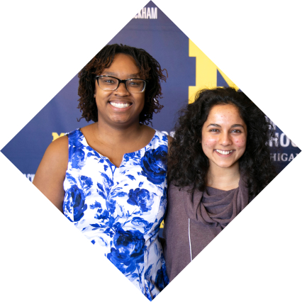 Two people pose for a photo in front of a U-M branded photo wall
