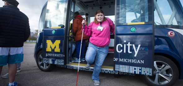 A blind person exits an M-City bus using their walking stick for guidance