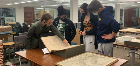 A group of people view a series of historic maps in a library setting