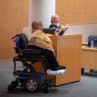 A woman in a wheelchair giving a presentation for a disability awareness event while another woman interprets the talk in sign language