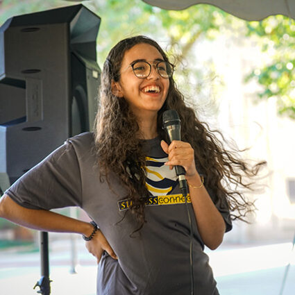 A student speaking into a microphone and wearing a SuccessConnects t-shirt