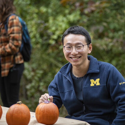 A student sitting and smiling with pumpkins at the SEAS annual campfire
